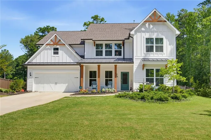 White board and batten exterior with dark trim accents, covered front porch with wood columns, attached two-car garage, and a lush green lawn