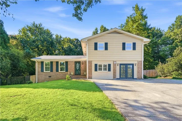 Split-level residence featuring a brick and siding exterior, a concrete driveway, an expansive lawn, and mature trees