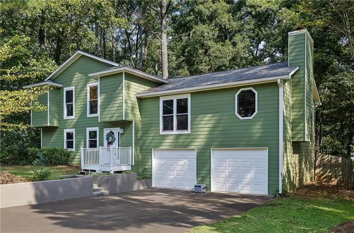 Two story residence with cement siding exterior, white porch railing, dual garage doors, and paved driveway