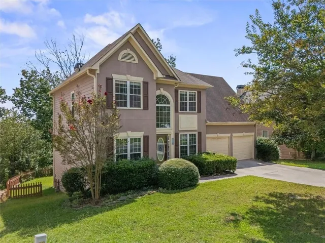 Two-story stucco and siding exterior with a prominent arched window, multi-pane windows with decorative shutters, a two-car garage, and established landscaping