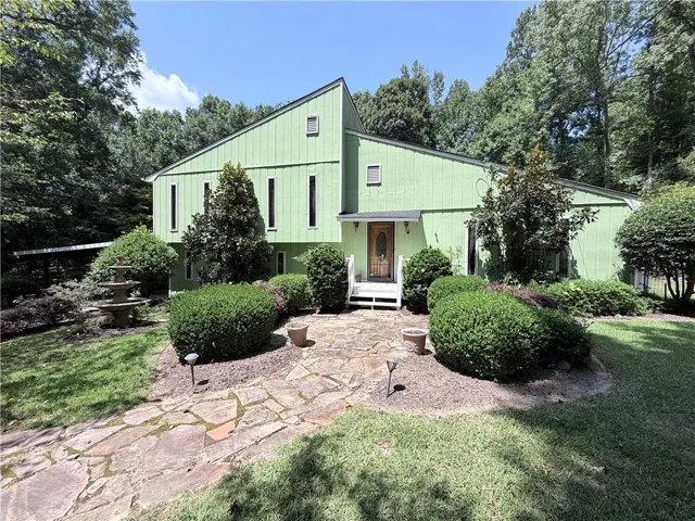 Contemporary exterior with a prominent asymmetrical roofline, a stone-paved walkway, tiered water feature, mature landscaping, and an ornate wooden front door