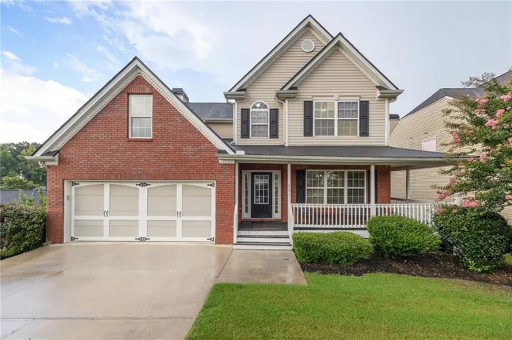 Two-story residence featuring a brick and siding exterior, a covered front porch with white railing, a two-car garage with decorative hardware, and a paved driveway