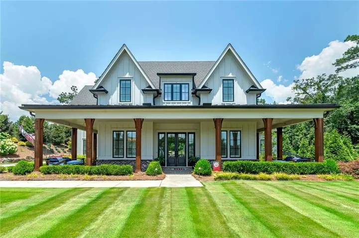 Modern farmhouse exterior with white board and batten siding, dark framed windows, a covered front porch with substantial wood pillars, and a stone foundation accent