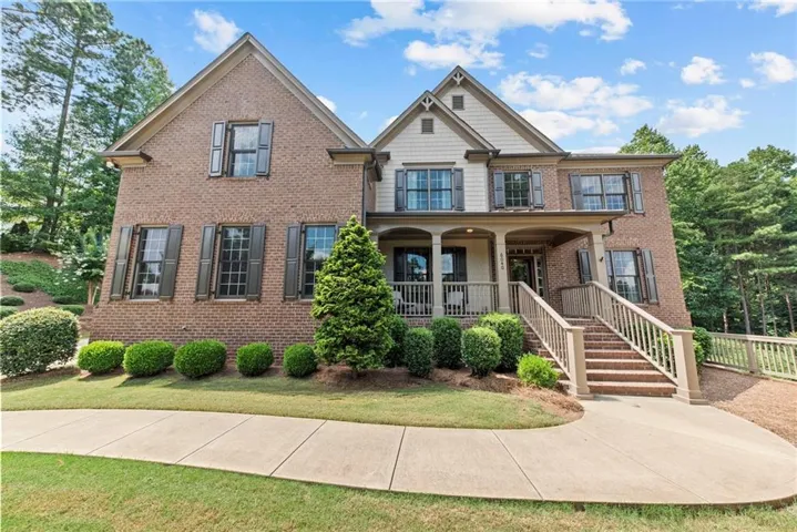 Brick exterior featuring multiple gables, shuttered windows, a covered front porch with columns, and a concrete walkway leading to a brick staircase with wood railings