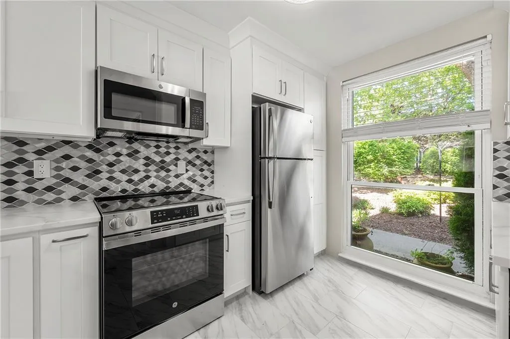 Kitchen with designer tiled backsplash  backsplash, white cabinetry, with soft close doors and drawers and new  appliances with smart oven. tiled floor, light quartz counters, Smart oven.
