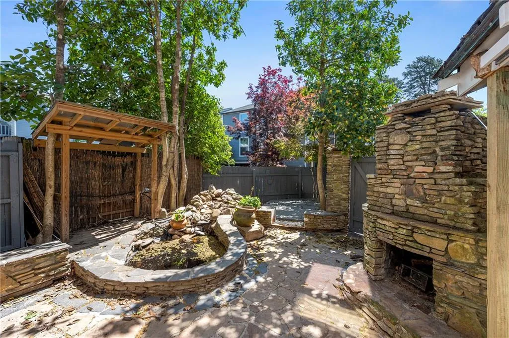 View of patio / terrace with a fenced backyard and an outdoor stone fireplace and pond