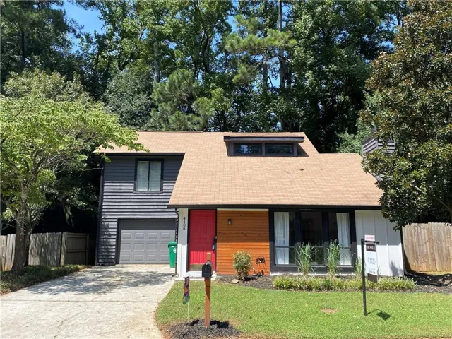 Split-level residence featuring a warm wood-tone siding accent, red entry door, attached garage, and a dormer window