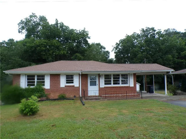 Brick ranch-style residence featuring a brown shingle roof, white window shutters, and a covered carport