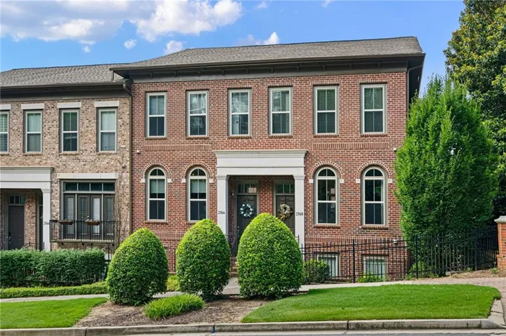 Brick facade townhome with arched ground-level windows, a covered entry, and a symmetrical front yard with manicured shrubs