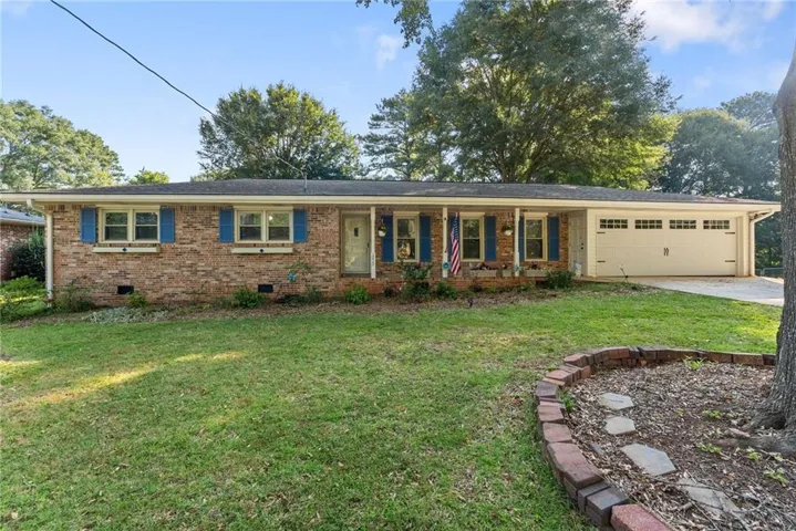 Brick exterior with a white garage door, featuring blue window shutters and a covered porch entry