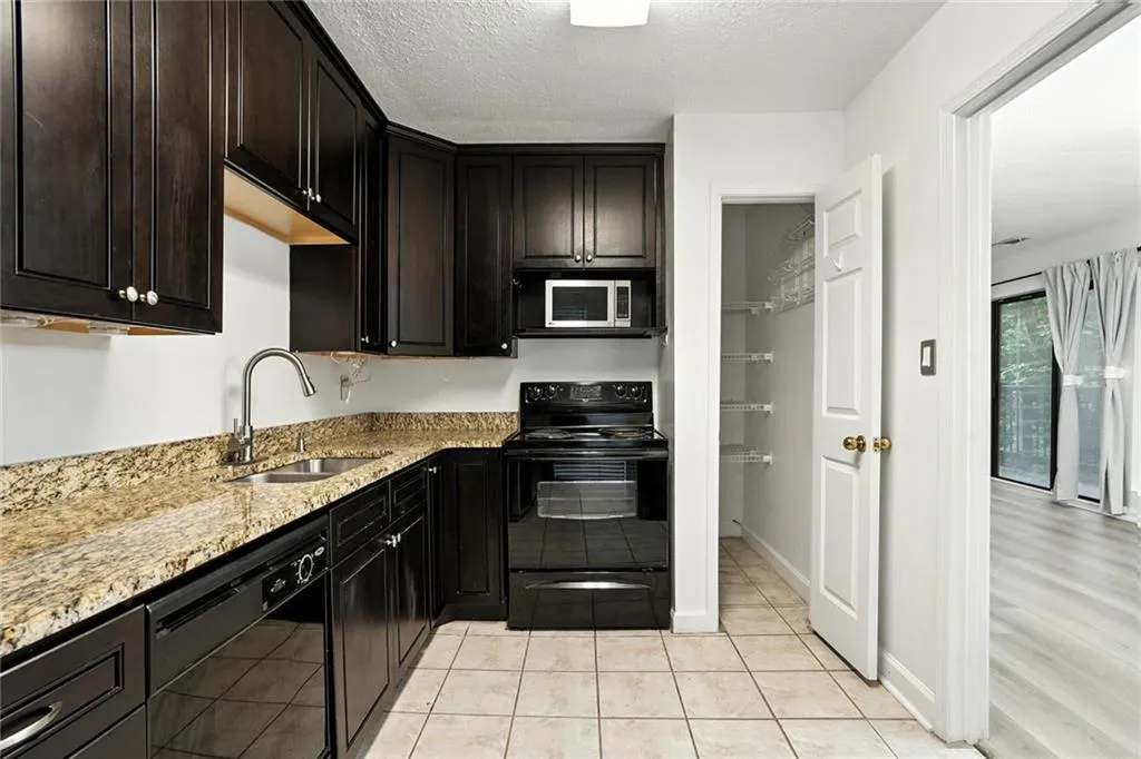Kitchen with black appliances, a textured ceiling, light stone countertops, and light tile patterned floors