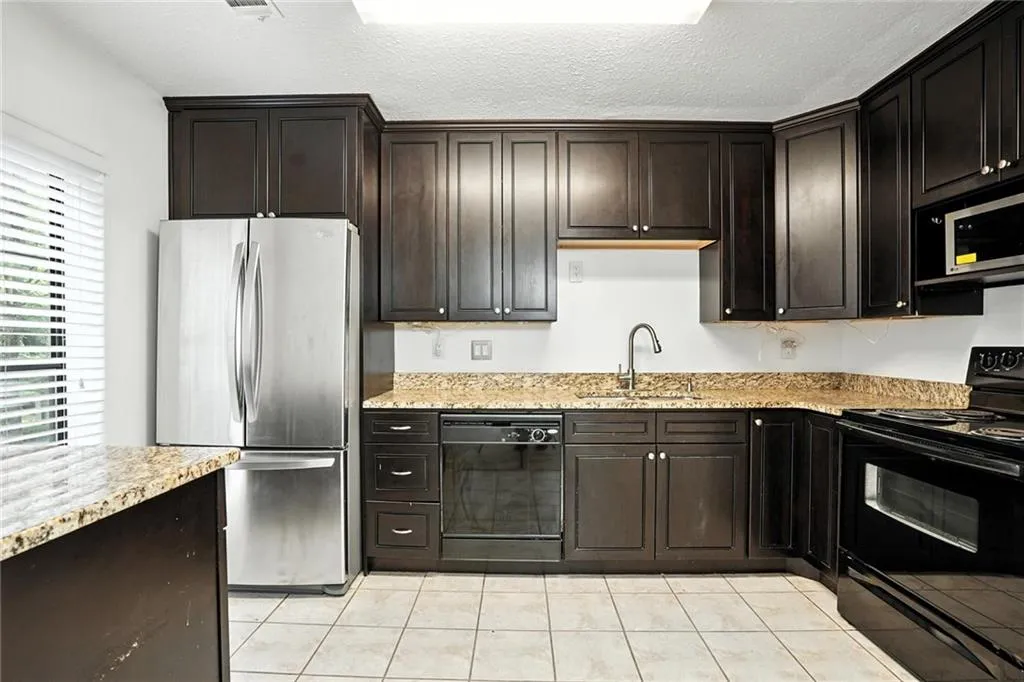 Kitchen featuring black appliances, light tile patterned floors, light stone countertops, a textured ceiling, and dark brown cabinetry