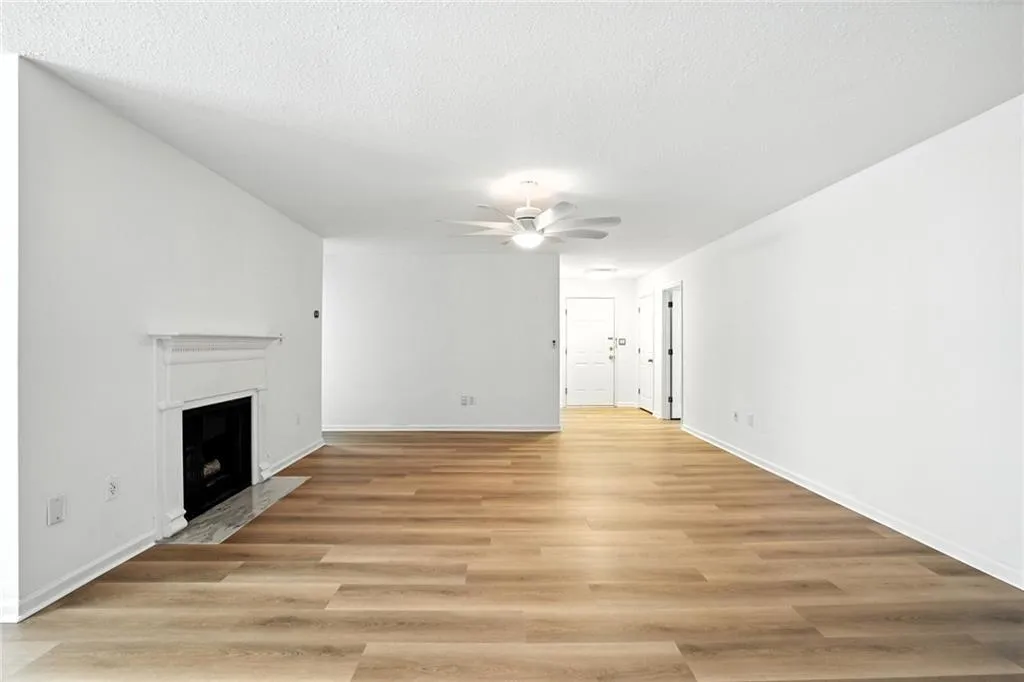 Unfurnished living room featuring light wood-style floors, a fireplace with flush hearth, a textured ceiling, and ceiling fan