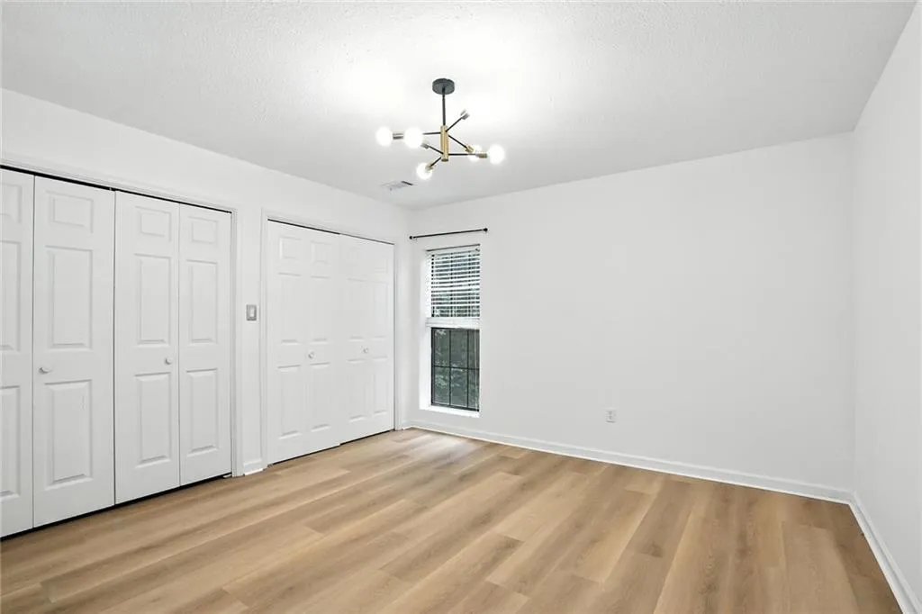 Unfurnished bedroom featuring two closets, light wood-style floors, a textured ceiling, and a chandelier