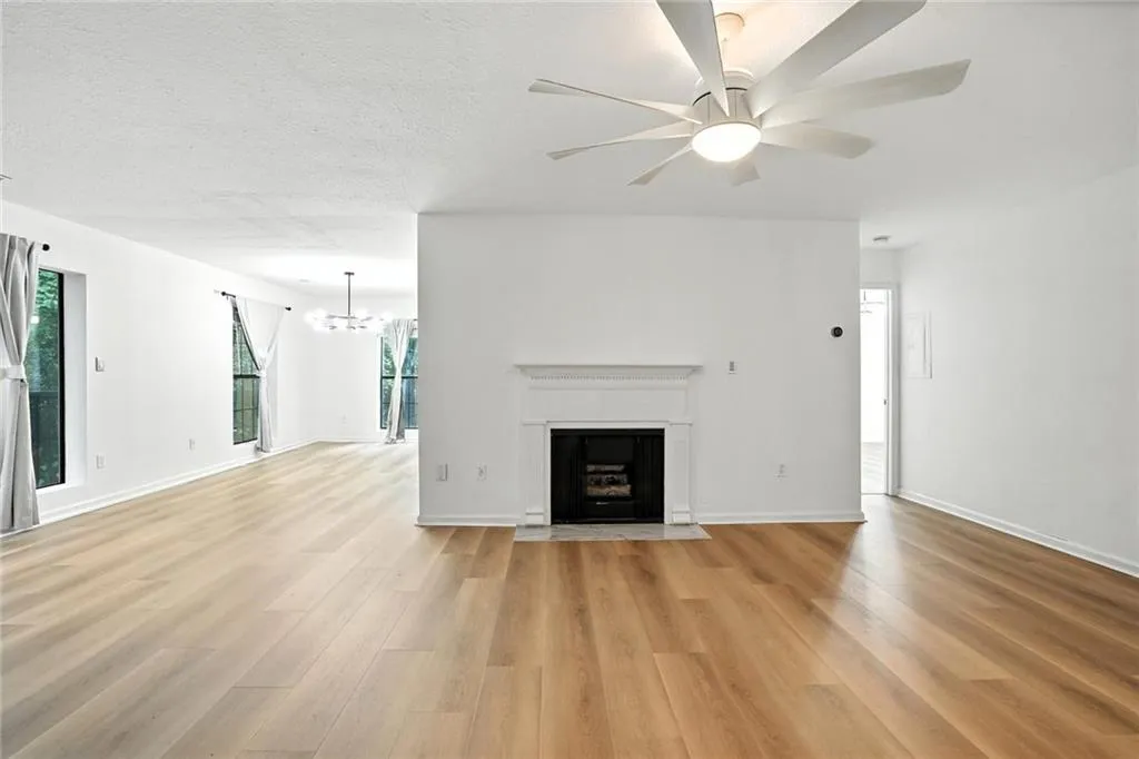 Unfurnished living room with a textured ceiling, a fireplace with flush hearth, light wood-style flooring, ceiling fan, and a chandelier
