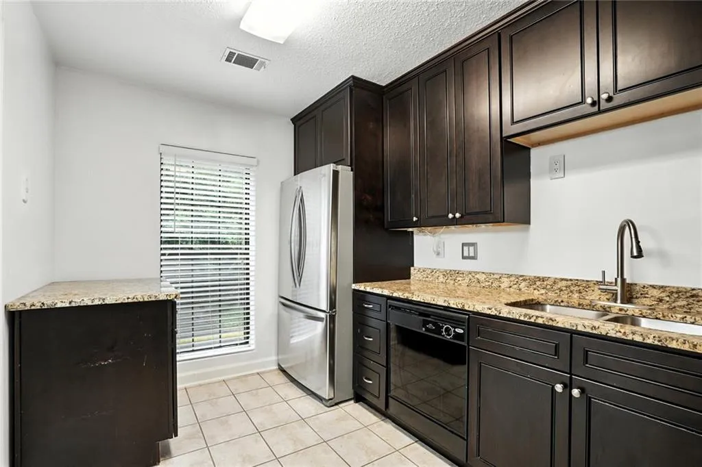Kitchen featuring light tile patterned flooring, dishwasher, freestanding refrigerator, light stone countertops, and a textured ceiling