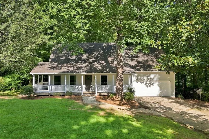 Exterior featuring a covered front porch, white railing, attached single-car garage, and a lush green lawn