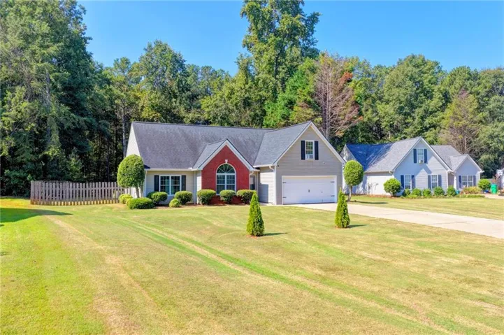 Expansive front lawn with mature landscaping, fenced perimeter, attached two-car garage, and a brick facade accent