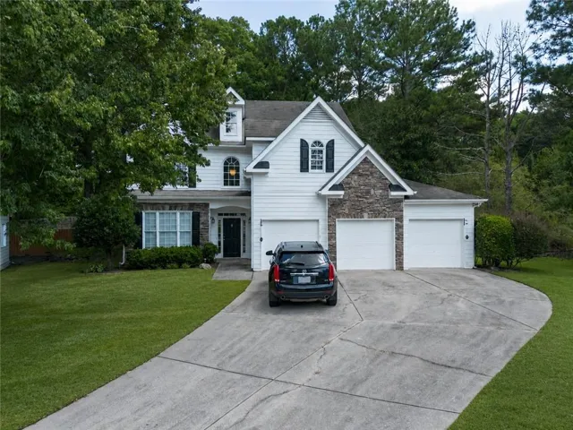 White siding exterior with stone accents, a three-car garage, dormer windows, a concrete driveway, and a front lawn