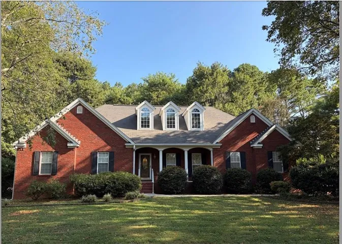 Red brick exterior featuring a covered entry, multiple dormer windows, and dark shutters