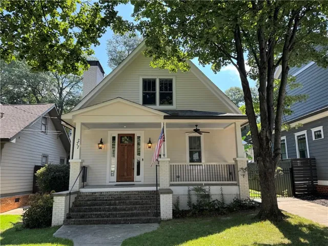 Cream-colored siding residence featuring a covered front porch with a ceiling fan, a dark wood entry door with glass panels, and exterior sconce lighting