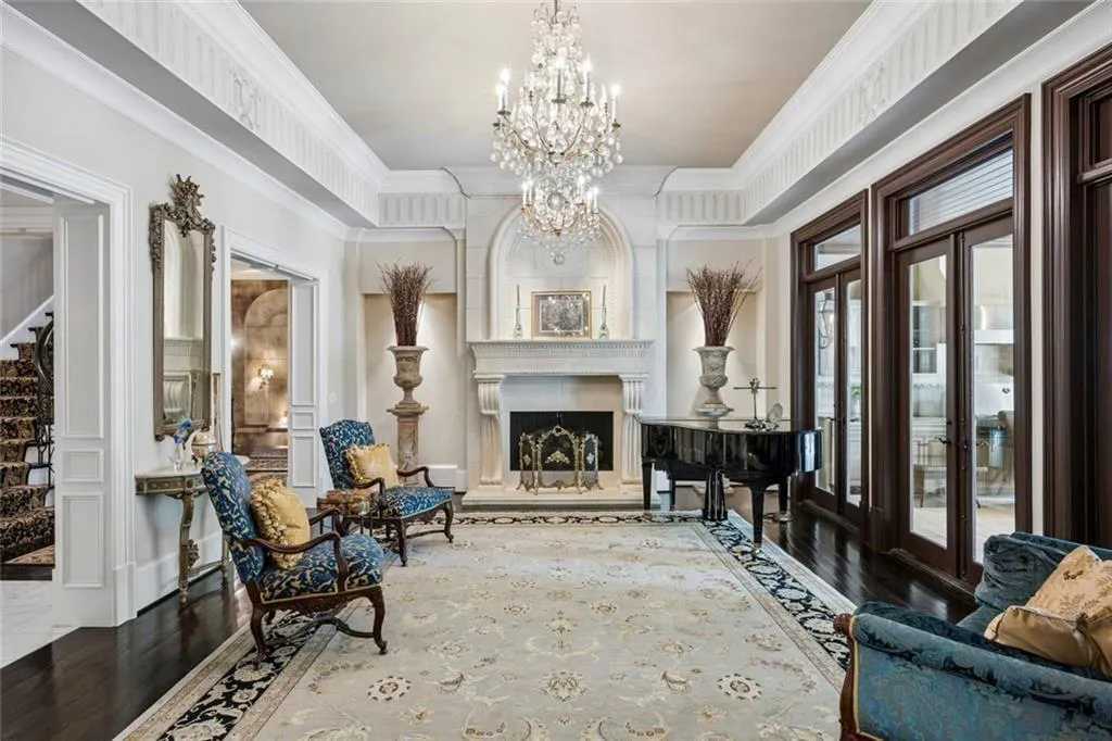 The formal living room makes a statement — a hand-carved limestone fireplace, crystal chandelier, and grand piano framed by walls of arched French doors leading to the veranda.