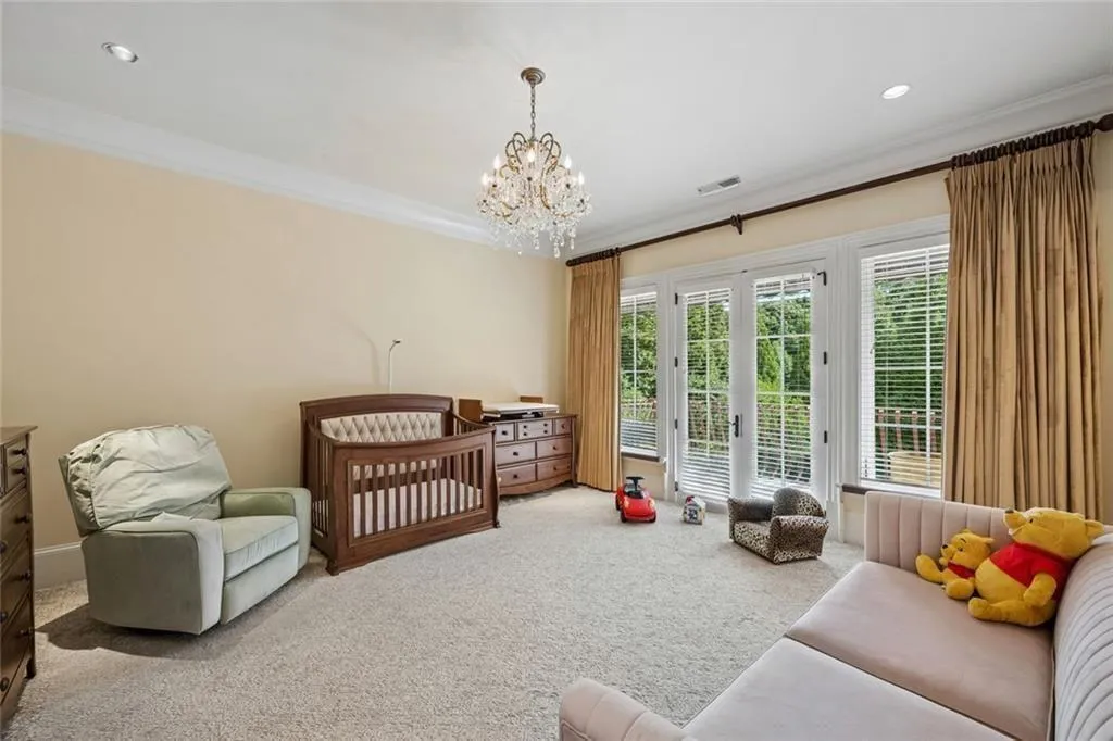 A spacious secondary bedroom with a crystal chandelier and French doors leading to a balcony.