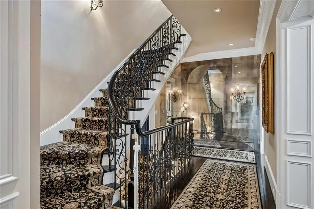 A sweeping curved staircase with custom wrought iron railings — opening onto a hall framed in antiqued mirror wall.