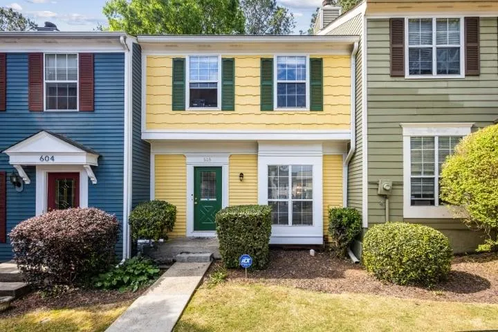 Two-story townhouse exterior featuring yellow siding with green shutters, a green entry door, and a white framed bay window
