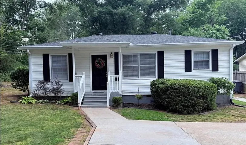 White siding exterior with a dark shingle roof, black shutters, and a covered porch entry