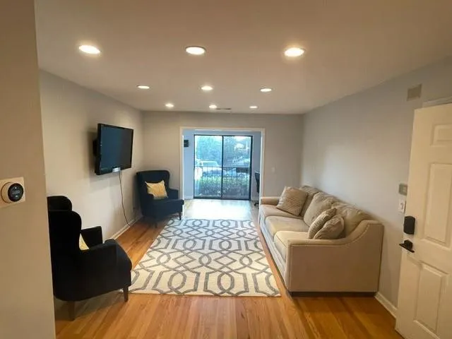 Recessed ceiling lighting, wood-finish flooring, light gray wall tones, and a sliding glass door