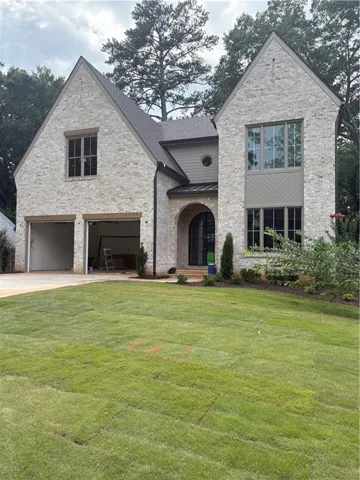 New construction residence featuring a light-colored brick exterior, a multi-gabled roofline, a prominent arched entry, a two-car garage, and a newly installed lawn