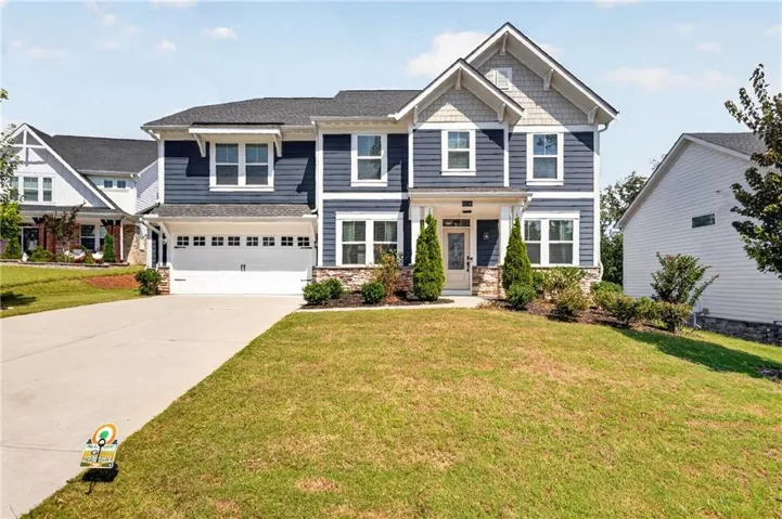 Two-story residence featuring blue siding, white trim, stone accents, a two-car garage, and a concrete driveway