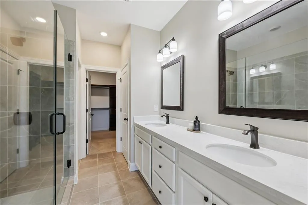 Bathroom with double vanity, a shower stall, light tile patterned floors, and a spacious closet