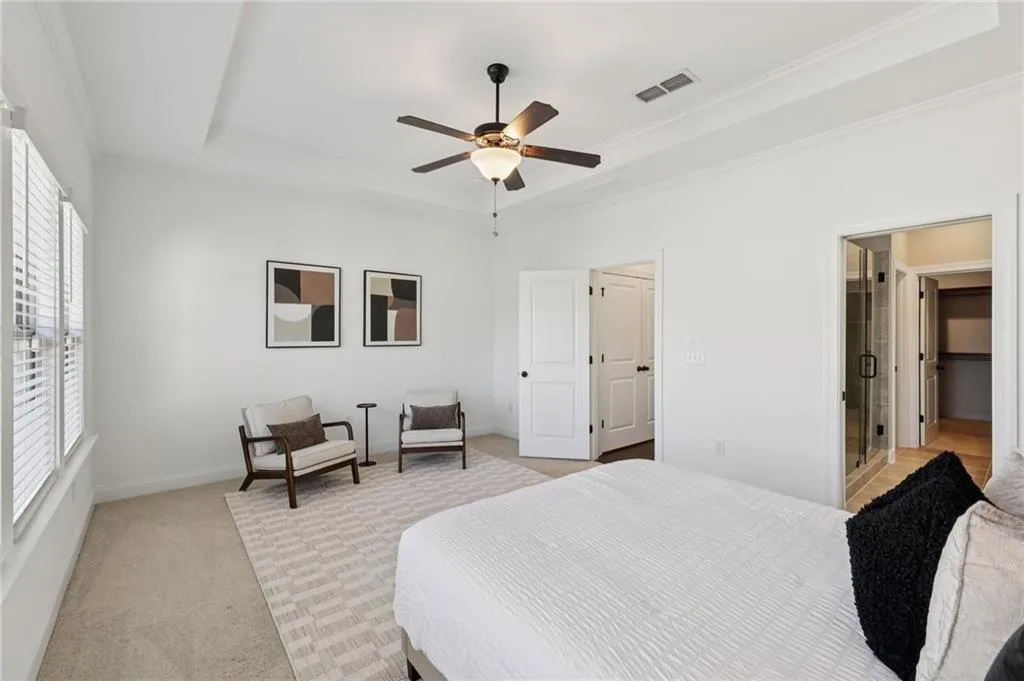 Bedroom featuring light colored carpet, a raised ceiling, ornamental molding, and ceiling fan