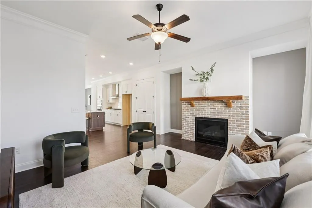 Living room featuring crown molding, ceiling fan, a brick fireplace, dark wood finished floors, and recessed lighting