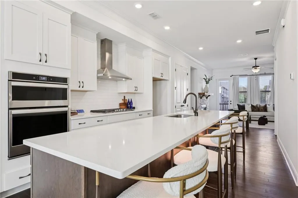 Dual tone kitchen with dark wood-type flooring, a kitchen island with sink, stainless steel appliances, light stone counters, and crown molding