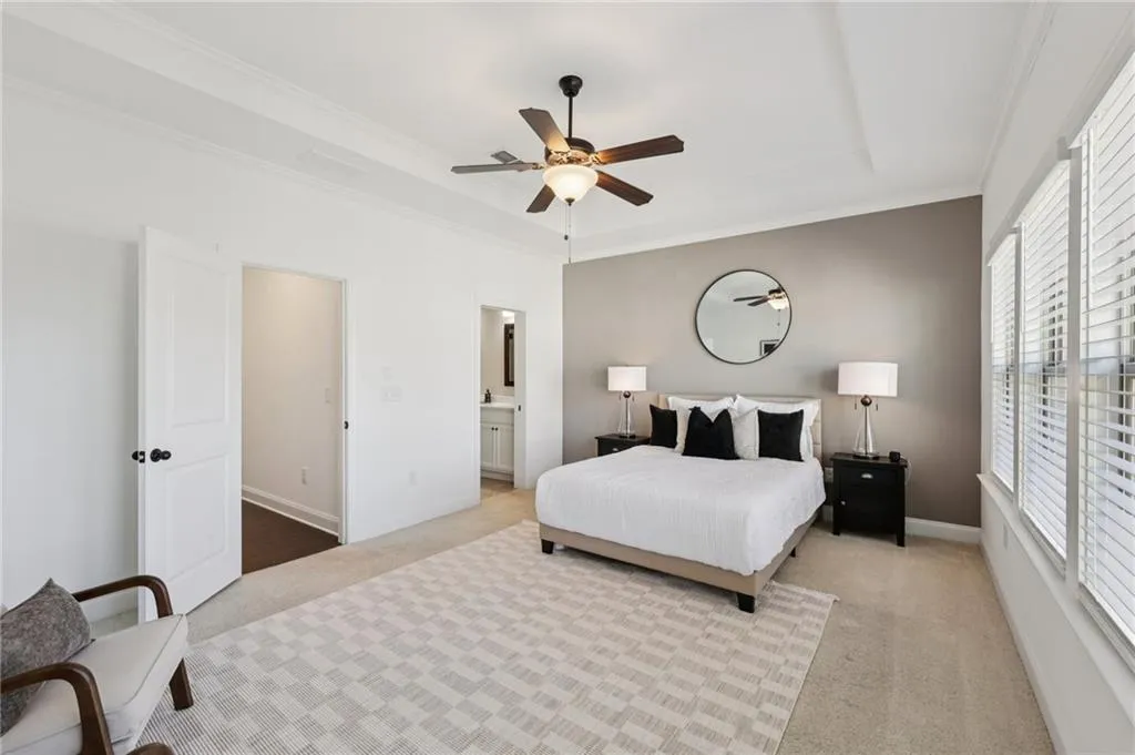 Bedroom featuring carpet floors, a raised ceiling, a ceiling fan, ornamental molding, and connected bathroom