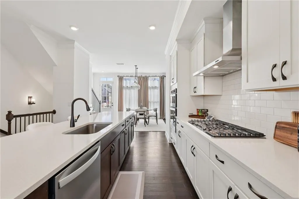 Kitchen featuring two tone cabinetry, crown molding, stainless steel appliances, dark wood-type flooring, and light stone counters