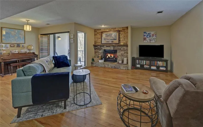 Living room featuring light wood finished floors, a textured ceiling, and a stone fireplace