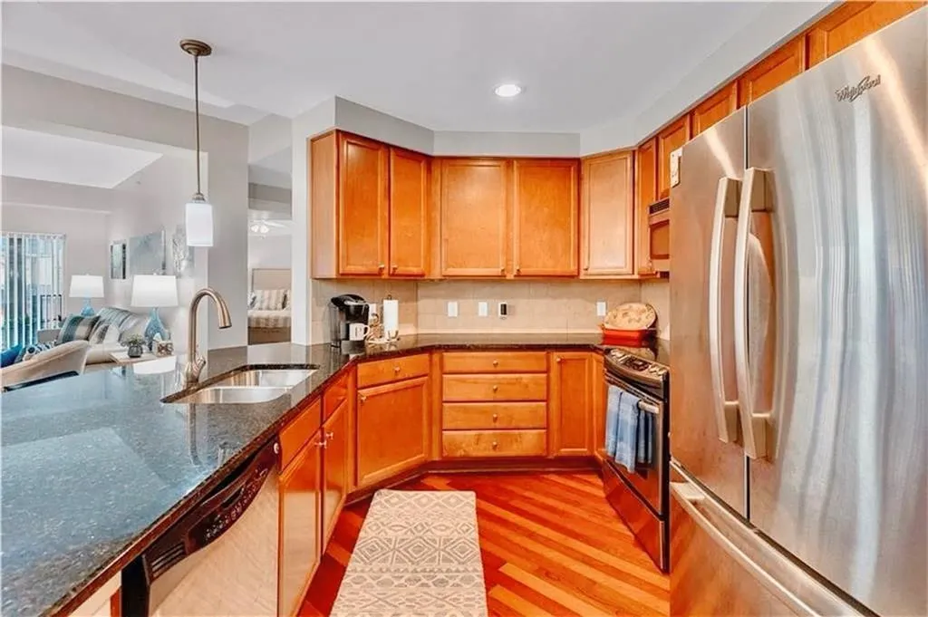 Kitchen with stainless steel appliances, dark stone countertops, wood finished floors, open floor plan, and hanging light fixtures