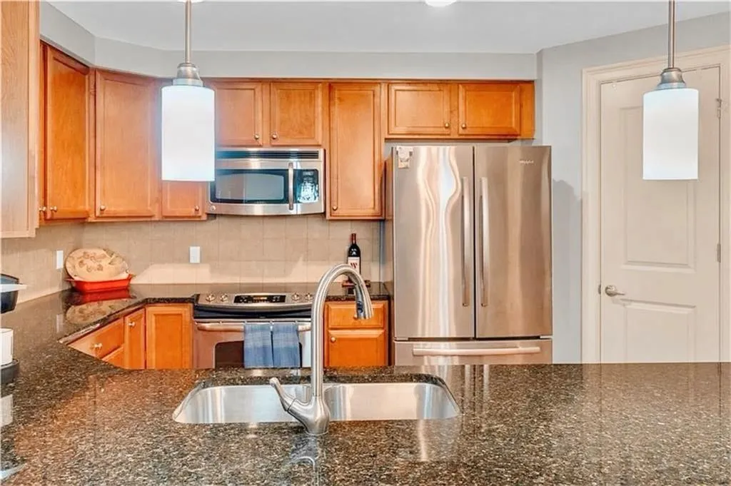 Kitchen with appliances with stainless steel finishes, decorative backsplash, dark stone counters, decorative light fixtures, and brown cabinetry
