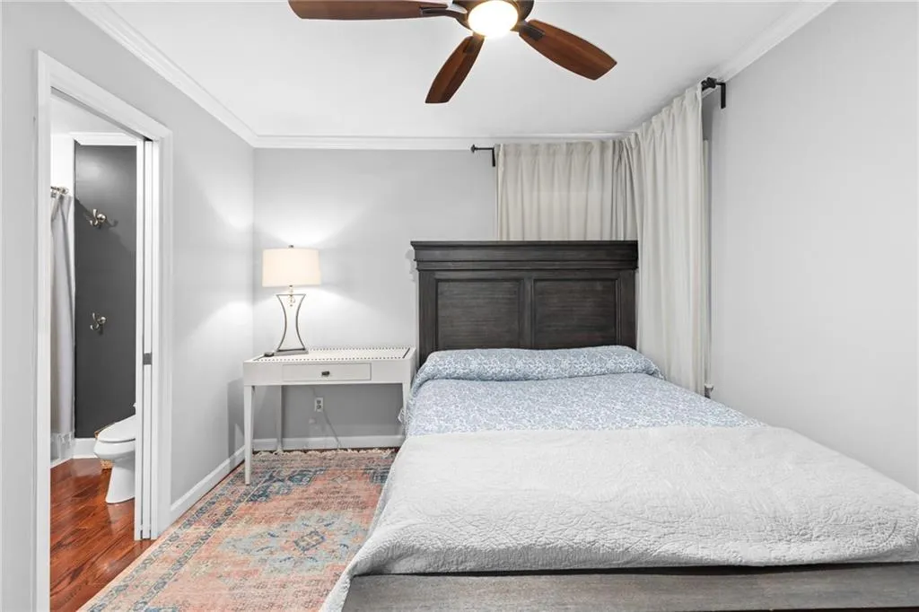Bedroom with crown molding, wood finished floors, ensuite bath, and ceiling fan