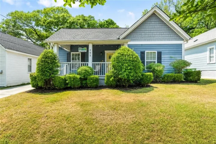 Blue exterior siding with white trim, covered front porch, white porch railing, front yard landscaping, and a pitched roof