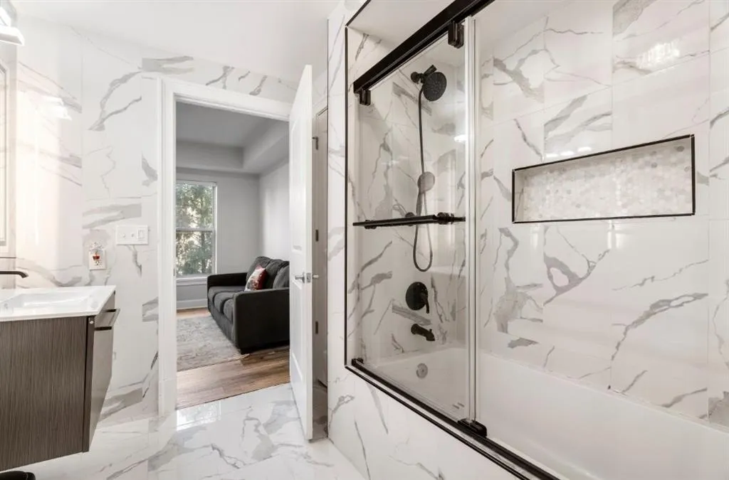 Ensuite bathroom featuring connected bathroom, bath / shower combo with glass door, stone wall, marble finish floor, and vanity