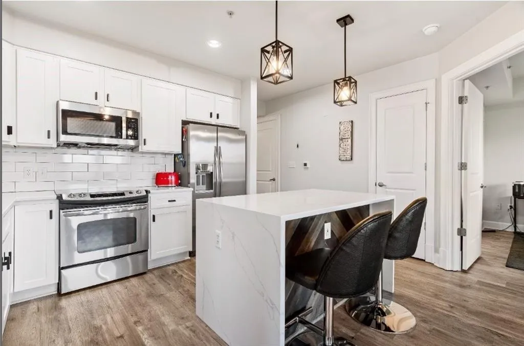 Kitchen with a kitchen breakfast bar, backsplash, light wood-type flooring, and appliances with stainless steel finishes