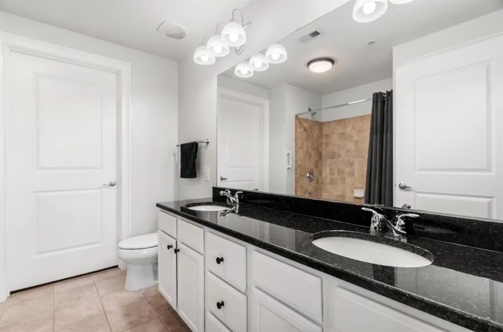 Primary suite with double vanity featuring tile patterned flooring, toilet and visible vents
