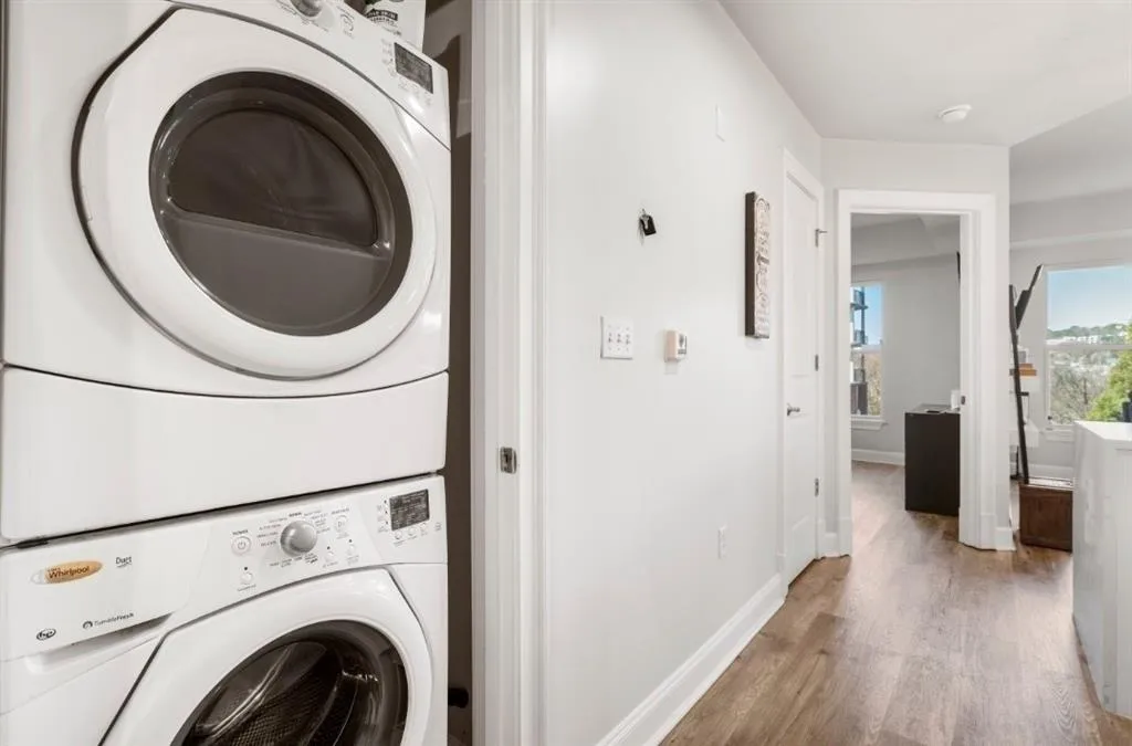 Laundry room with laundry area, baseboards, light wood finished floors, and stacked washing maching and dryer