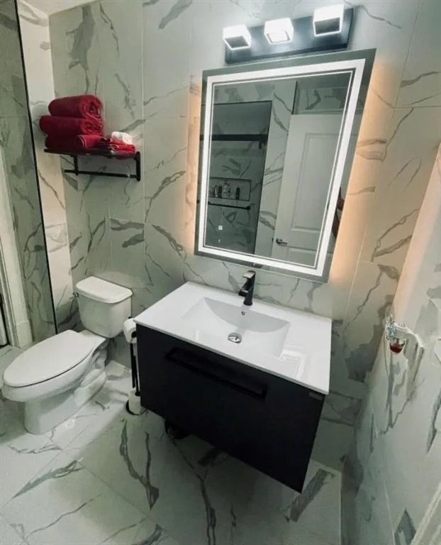 Bathroom featuring vanity, stone wall, toilet, and marble finish floor