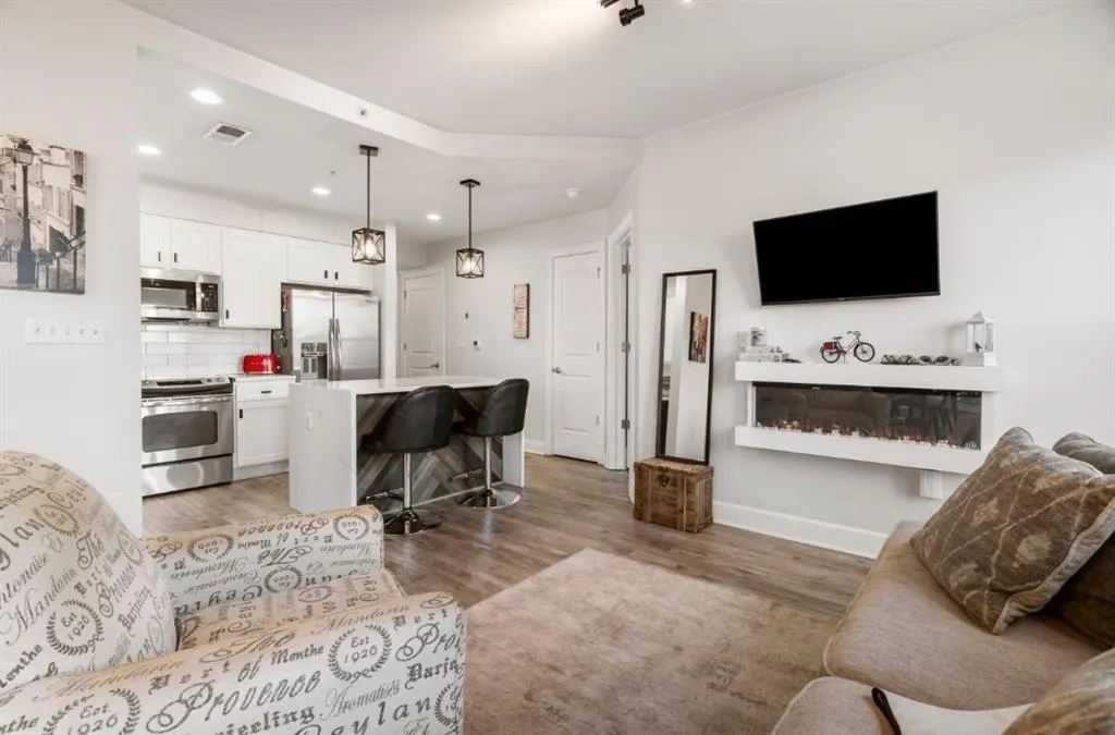 Living room with light wood finished floors, visible vents, baseboards, recessed lighting, and a glass covered fireplace